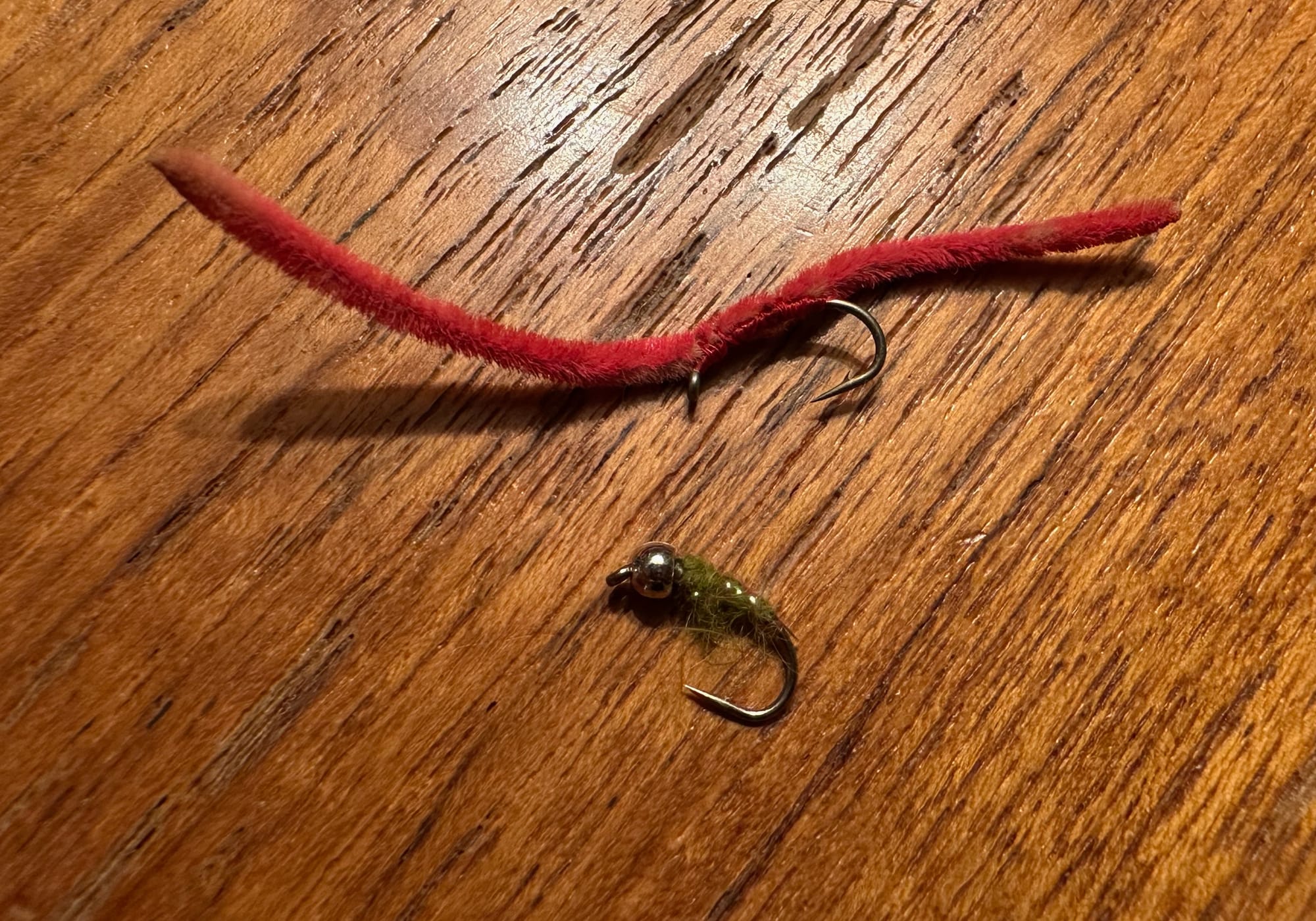 Two fly-fishing flies on a wooden table: a San Juan worm and a caddis nymph.